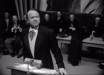 Movie still from “Citizen Kane” (1941), directed by Orson Welles – A black and white photo of a man speaking at a podium; Medium shot, Low angle