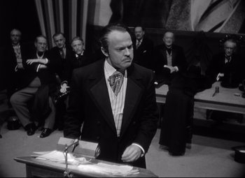 Movie still from “Citizen Kane” (1941), directed by Orson Welles – A man standing at a podium in front of a group of people; Medium shot, Low angle