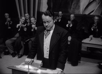 Movie still from “Citizen Kane” (1941), directed by Orson Welles – A black and white photo of a man at a podium; Medium shot, Over the shoulder angle