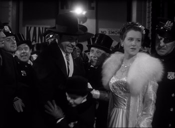 Movie still from “Citizen Kane” (1941), directed by Orson Welles – A man and a woman are standing in front of a group of people; Medium shot, Low angle