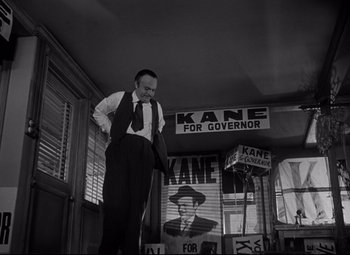 Movie still from “Citizen Kane” (1941), directed by Orson Welles – A black and white photo of a man standing in front of a sign; Medium shot, Low angle