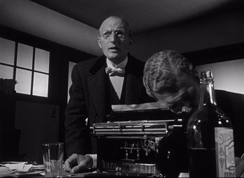 Movie still from “Citizen Kane” (1941), directed by Orson Welles – An older man in a suit and bow tie is looking at a typewriter while a younger man looks on; Medium shot, Low angle
