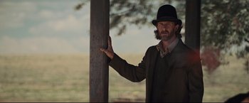 Movie still from “Cowboys & Aliens” (2011), directed by Jon Favreau – A man wearing a hat standing next to a wooden pole; Medium shot, Low angle