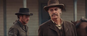 Movie still from “Cowboys & Aliens” (2011), directed by Jon Favreau – A man in a brown suit and a brown hat standing next to another man in a brown suit; Close Up shot, Over the shoulder angle