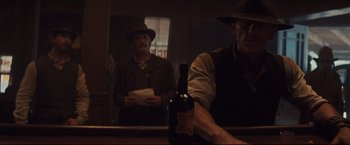 Movie still from “Cowboys & Aliens” (2011), directed by Jon Favreau – A man in a hat is holding a bottle of wine; Medium shot, Low angle