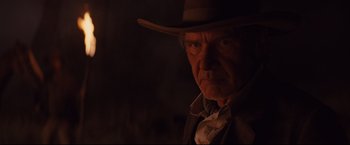 Movie still from “Cowboys & Aliens” (2011), directed by Jon Favreau – An older man wearing a cowboy hat in a dimly - lit room; Close Up shot, Low angle