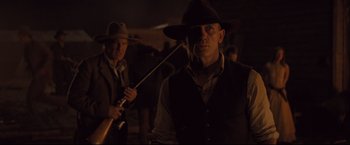 Movie still from “Cowboys & Aliens” (2011), directed by Jon Favreau – A man with a hat and a whip in a dark room; Medium shot, Over the shoulder angle