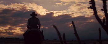 Movie still from “Cowboys & Aliens” (2011), directed by Jon Favreau – A person riding a horse in a field at sunset; Wide shot, Low angle