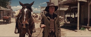 Movie still from “Cowboys & Aliens” (2011), directed by Jon Favreau – A young man in a cowboy hat is leading a horse; Medium shot, Low angle