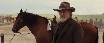 Movie still from “Cowboys & Aliens” (2011), directed by Jon Favreau – An older man with a beard is standing next to a horse; Medium shot, Over the shoulder angle