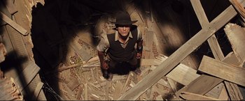 Movie still from “Cowboys & Aliens” (2011), directed by Jon Favreau – A man sitting on the ground holding a gun; Wide shot, Overhead angle