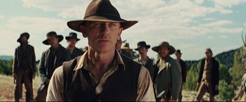 Movie still from “Cowboys & Aliens” (2011), directed by Jon Favreau – A man in a hat standing in front of other men; Close Up shot, Over the shoulder angle