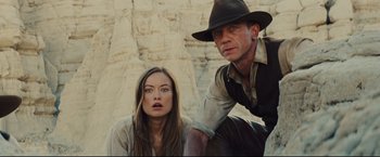 Movie still from “Cowboys & Aliens” (2011), directed by Jon Favreau – A man and a woman are standing next to each other in front of a cliff; Medium shot, Low angle