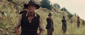Movie still from “Cowboys & Aliens” (2011), directed by Jon Favreau – A man in a cowboy hat and vest standing in a grassy field; Medium shot, Low angle