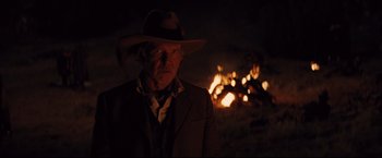 Movie still from “Cowboys & Aliens” (2011), directed by Jon Favreau – A man wearing a hat standing in front of a fire; Medium shot, Over the shoulder angle