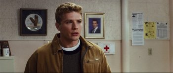 Movie still from “Crash” (2004), directed by Paul Haggis – A man standing in front of a wall with a picture of himself; Medium shot, Over the shoulder angle