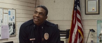 Movie still from “Crash” (2004), directed by Paul Haggis – A police officer smiling for the camera in his uniform; Close Up shot, High angle