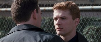 Movie still from “Crash” (2004), directed by Paul Haggis – Two young men standing next to each other near a chain link fence; Close Up shot, Over the shoulder angle