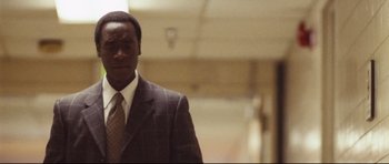 Movie still from “Crash” (2004), directed by Paul Haggis – A man wearing a suit and tie standing in a room; Medium shot, Over the shoulder angle