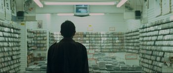Movie still from “Crash” (2004), directed by Paul Haggis – A man standing in front of a wall full of cds; Medium shot, Over the shoulder angle
