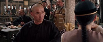 Movie still from “Crouching Tiger, Hidden Dragon” (2000), directed by Ang Lee – A man with a shaved head is sitting in front of a group of people; Close Up shot, Over the shoulder angle