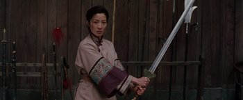 Movie still from “Crouching Tiger, Hidden Dragon” (2000), directed by Ang Lee – A woman holding a sword in front of a wooden fence; Medium shot, Low angle