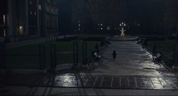 Movie still from “Cruella” (2021), directed by Craig Gillespie – People walking on a sidewalk at night near a fountain; Extreme Wide shot, High angle