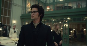 Movie still from “Cruella” (2021), directed by Craig Gillespie – A man and a woman standing next to each other in front of a building; Medium shot, Low angle