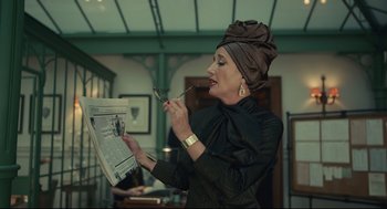 Movie still from “Cruella” (2021), directed by Craig Gillespie – A woman in a head scarf is holding a spoon and reading a newspaper; Medium shot, Low angle