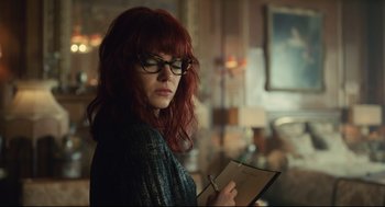 Movie still from “Cruella” (2021), directed by Craig Gillespie – A woman with red hair and glasses holding a notebook; Close Up shot, Over the shoulder angle
