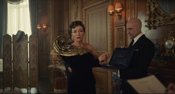 Movie still from “Cruella” (2021), directed by Craig Gillespie – A woman in a black dress holding a laptop; Medium shot, Over the shoulder angle