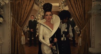 Movie still from “Cruella” (2021), directed by Craig Gillespie – A woman in a white dress with a black hat on her head; Medium shot, Low angle