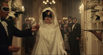 Movie still from “Cruella” (2021), directed by Craig Gillespie – A woman in a white dress and black mask; Medium shot, Over the shoulder angle