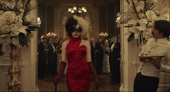 Movie still from “Cruella” (2021), directed by Craig Gillespie – A woman in a long red dress with a white mask and a white feather in her hair; Medium shot, Over the shoulder angle