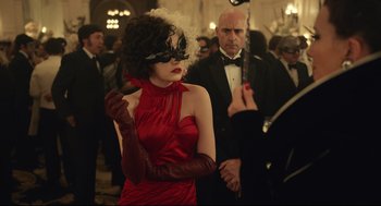 Movie still from “Cruella” (2021), directed by Craig Gillespie – A woman in a red dress wearing a black mask; Medium shot, Over the shoulder angle
