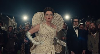 Movie still from “Cruella” (2021), directed by Craig Gillespie – A woman in a white dress and white gloves standing in front of a group of people; Medium shot, Low angle