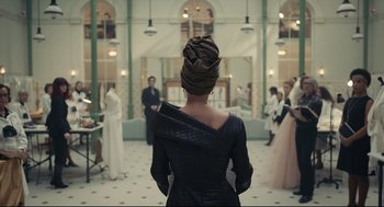Movie still from “Cruella” (2021), directed by Craig Gillespie – A woman in a black dress with a head scarf on; Medium shot, Over the shoulder angle