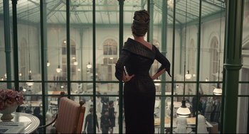 Movie still from “Cruella” (2021), directed by Craig Gillespie – A woman standing in front of a large glass window; Wide shot, Over the shoulder angle