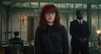 Movie still from “Cruella” (2021), directed by Craig Gillespie – A woman with red hair and glasses standing in a room; Medium shot, Low angle