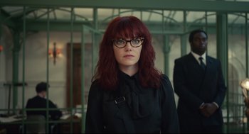 Movie still from “Cruella” (2021), directed by Craig Gillespie – A woman with red hair wearing glasses and a black shirt; Medium shot, Low angle