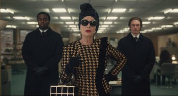 Movie still from “Cruella” (2021), directed by Craig Gillespie – A woman in a houndstooth dress and a turban; Medium shot, Over the shoulder angle