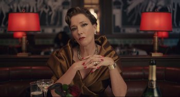 Movie still from “Cruella” (2021), directed by Craig Gillespie – A woman sitting at a table with her hands crossed; Medium shot, Low angle