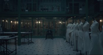 Movie still from “Cruella” (2021), directed by Craig Gillespie – A man sitting in front of a row of mannequins in a room; Wide shot, High angle