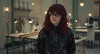 Movie still from “Cruella” (2021), directed by Craig Gillespie – A woman with red hair wearing glasses and a black shirt; Close Up shot, Over the shoulder angle