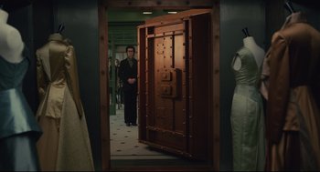 Movie still from “Cruella” (2021), directed by Craig Gillespie – A man standing in front of an open door in a room; Wide shot, High angle