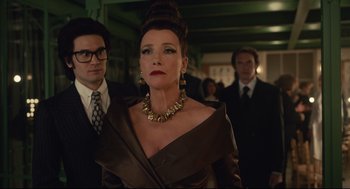 Movie still from “Cruella” (2021), directed by Craig Gillespie – A woman in a brown dress and a man in a black suit; Medium shot, Over the shoulder angle
