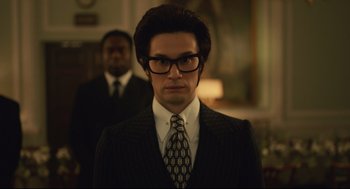 Movie still from “Cruella” (2021), directed by Craig Gillespie – A man in a suit and tie wearing glasses; Close Up shot, Low angle