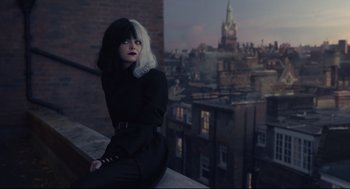 Movie still from “Cruella” (2021), directed by Craig Gillespie – A woman sitting on a ledge in front of a city skyline; Medium shot, High angle