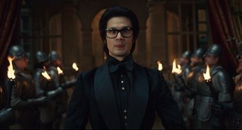 Movie still from “Cruella” (2021), directed by Craig Gillespie – A man in a black suit standing in front of fire; Medium shot, Low angle