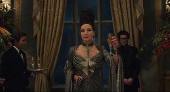 Movie still from “Cruella” (2021), directed by Craig Gillespie – A woman holding a wine glass in front of a window; Medium shot, Low angle
